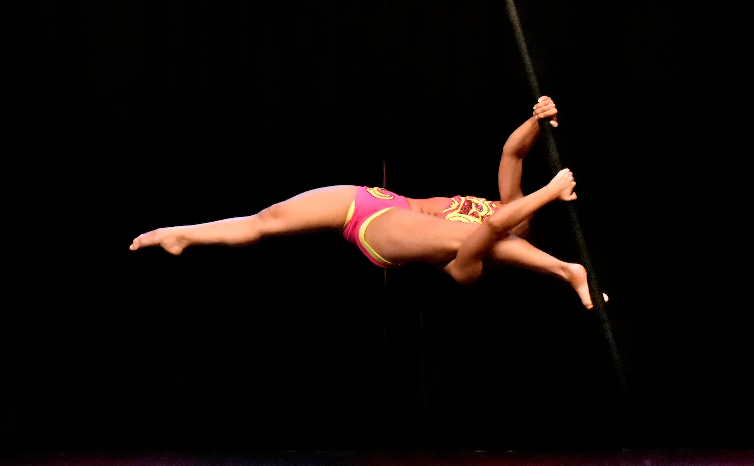 mulher executando movimento do pole dance que exige muita força e alongamento